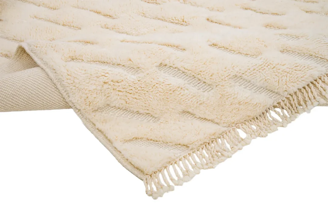 Close-up of a beige textured rug with a fringe on the edge, partially folded over.