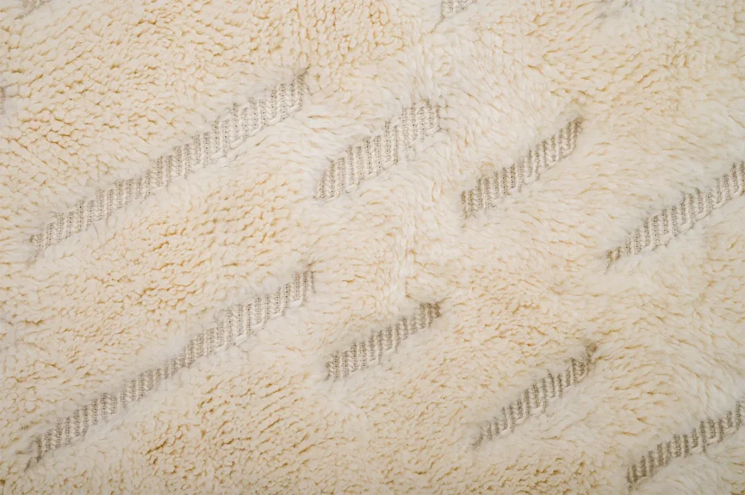 Close-up of a textured beige fabric with a zigzag pattern and raised, fluffy threads.