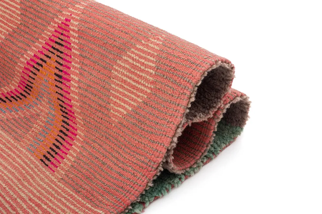 Folded woven textile in shades of pink, red, and orange with multicolored geometric patterns.