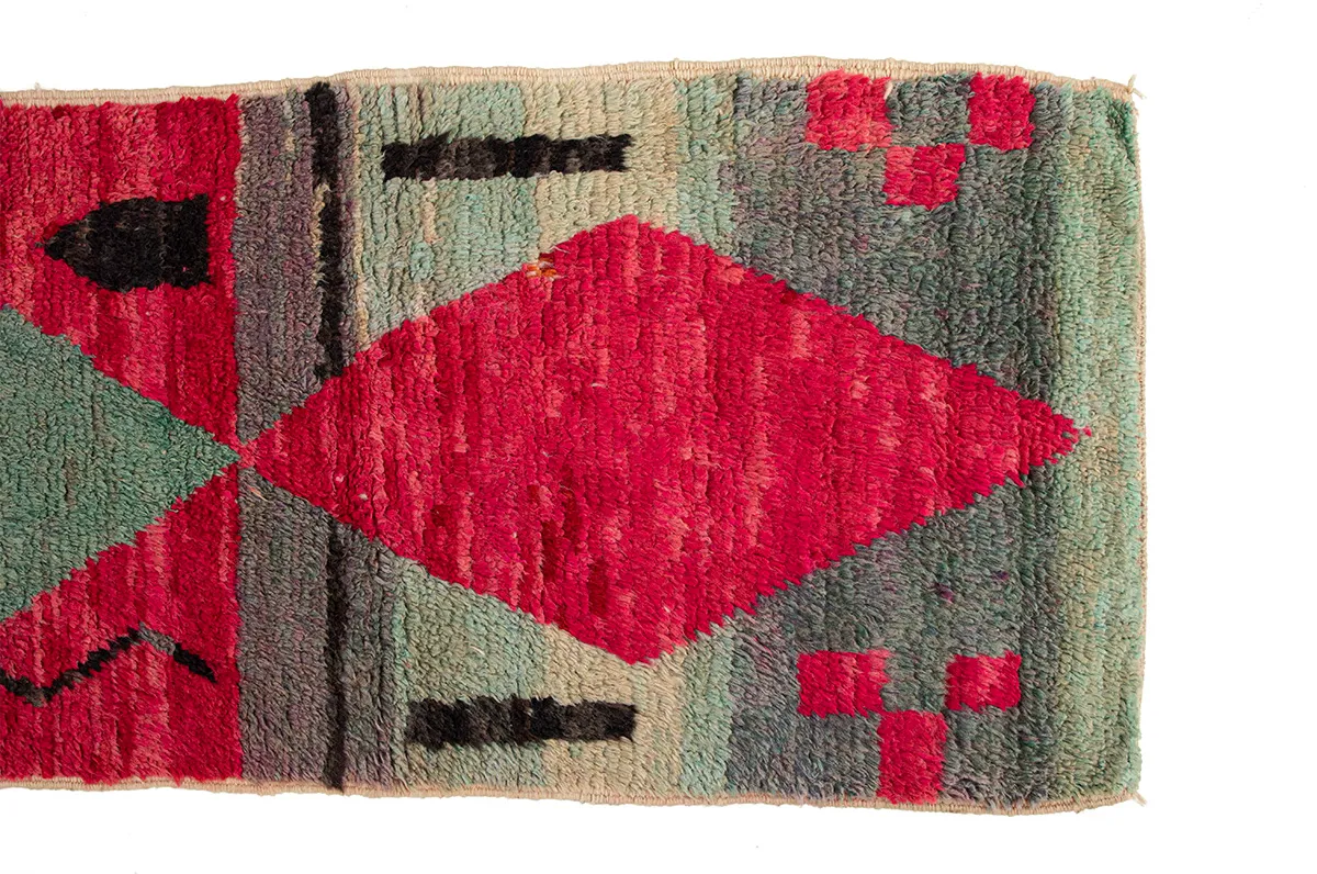 A rectangular rug with geometric patterns featuring red, black, and green colors, including a large central diamond shape on the left and smaller shapes on the right.