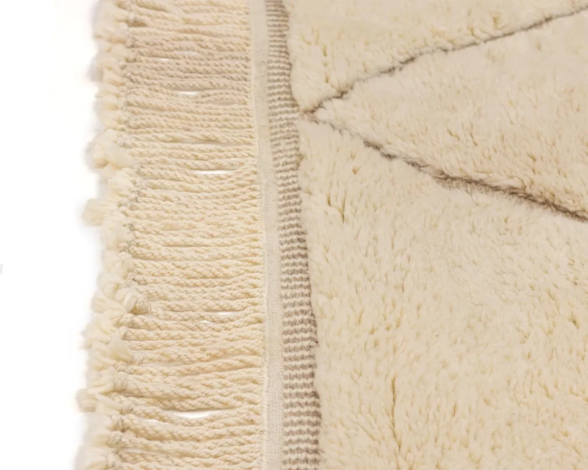 Close-up of a beige fluffy rug with tassels on one side and a textured pattern on the other.