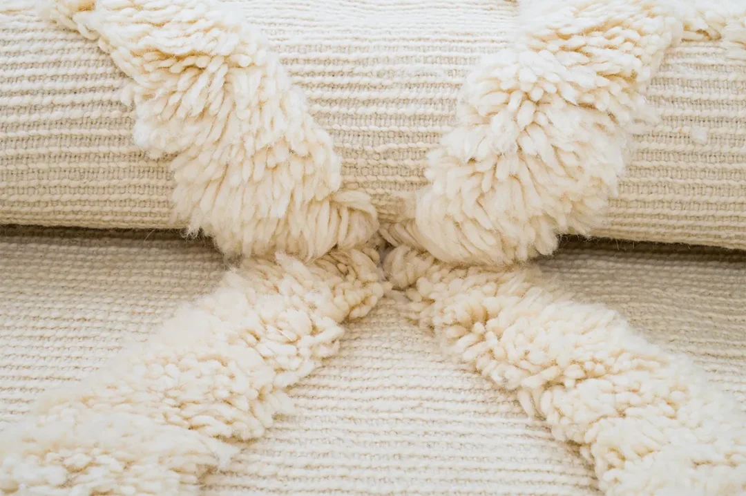 Close-up of cream-colored knotted rug with thick, raised, fluffy stripes forming an X pattern on the surface.