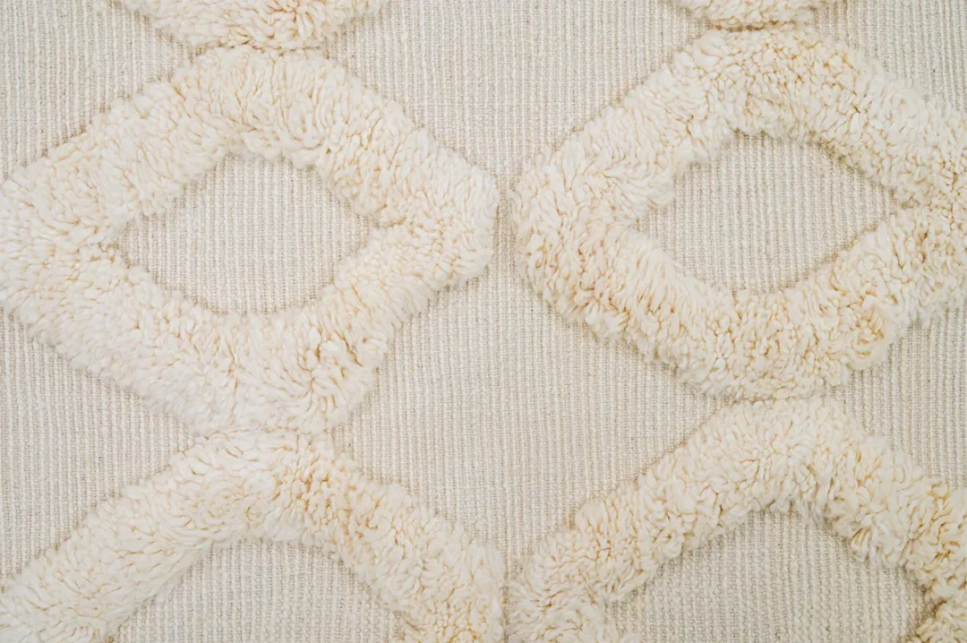 A close-up of a textured beige fabric with a geometric diamond pattern made of raised, fluffy material.