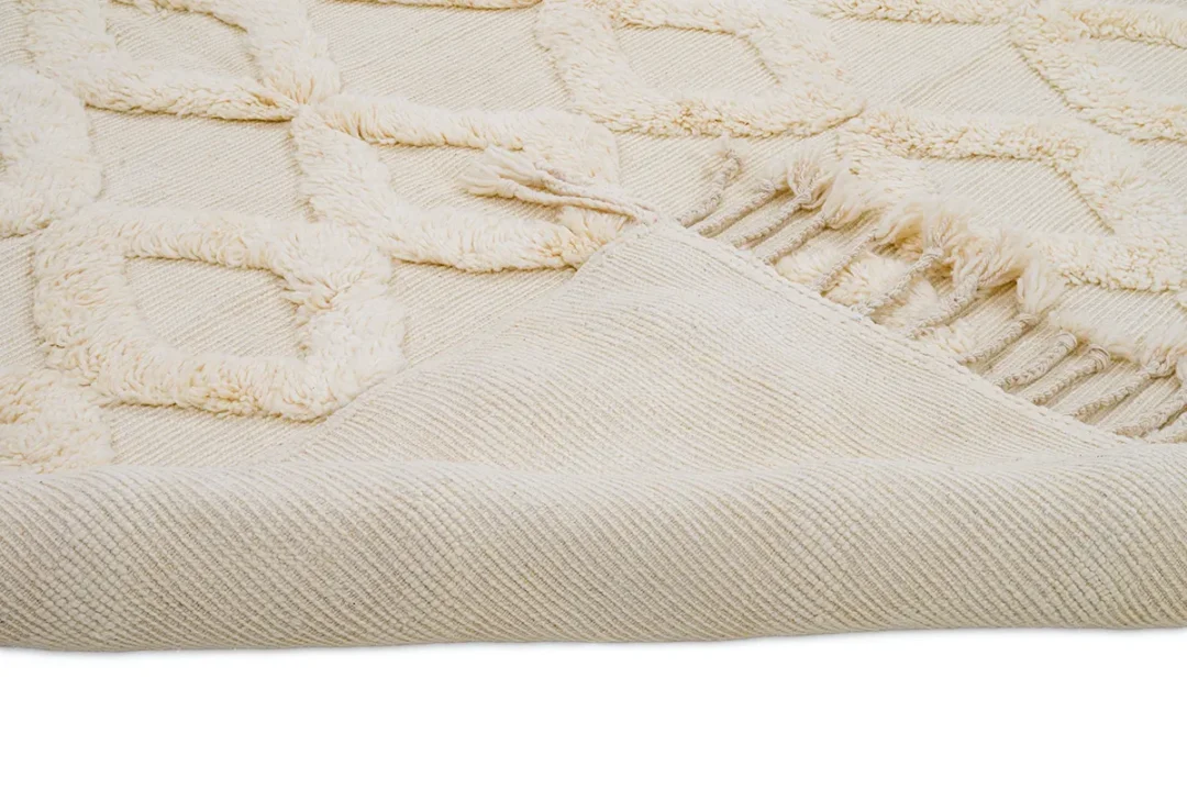 A close-up of a cream-colored textured rug with geometric patterns and a folded corner revealing the underside.