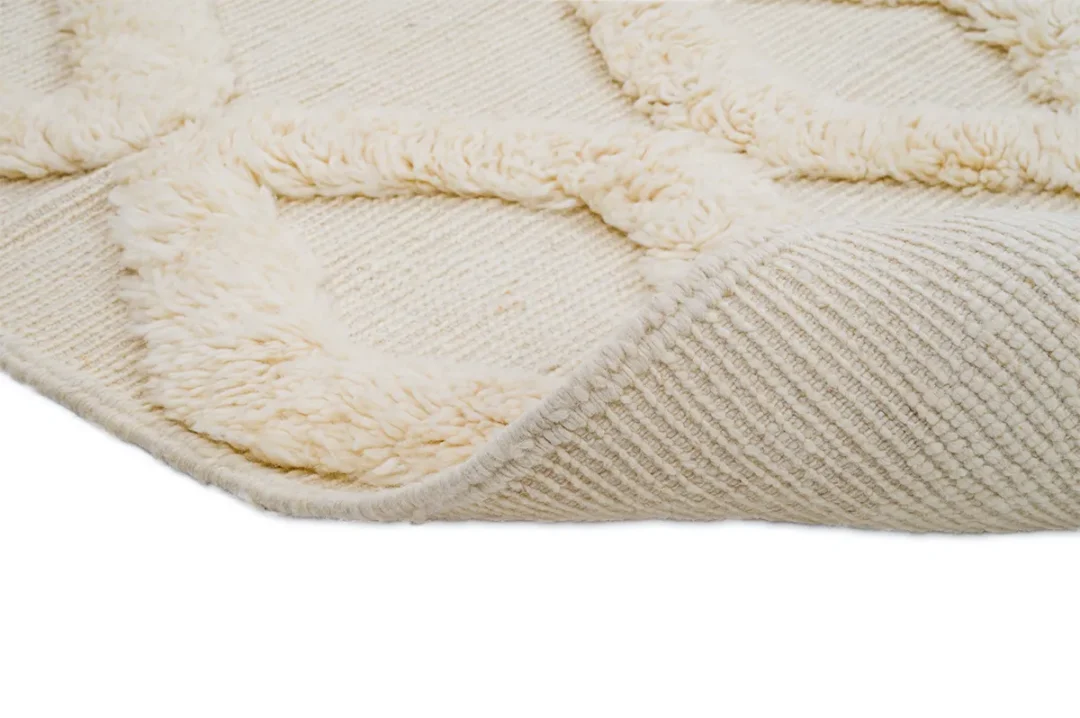 Close-up of a cream-colored textured rug corner showing raised geometric patterns and the woven underside.