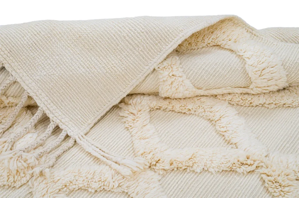 A close-up of a cream-colored textured throw blanket with fringe ends and a geometric tufted pattern.