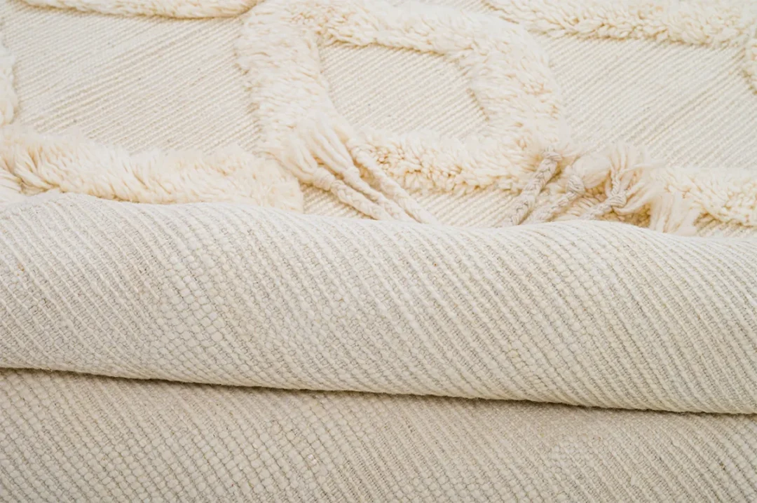 Close-up of a rolled beige textured rug with a geometric pattern on the visible surface.