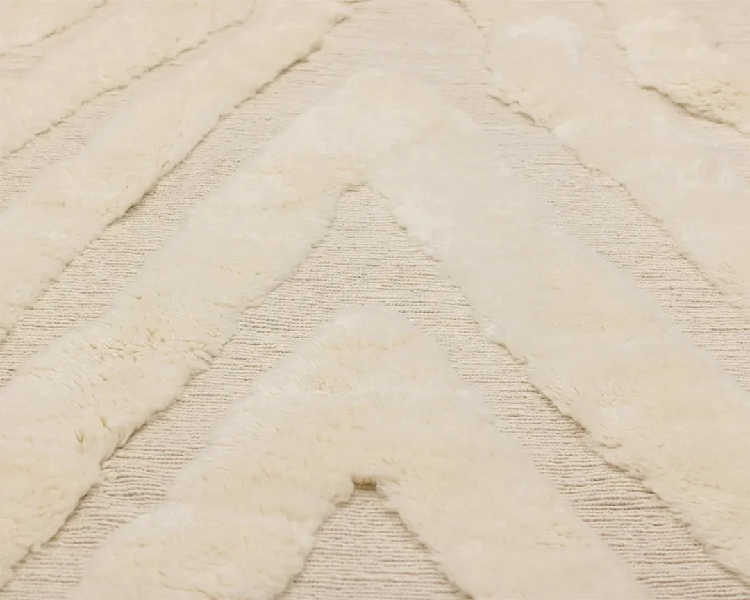 A close-up of a cream-colored textured rug with soft, raised chevron patterns on a flat, woven background.