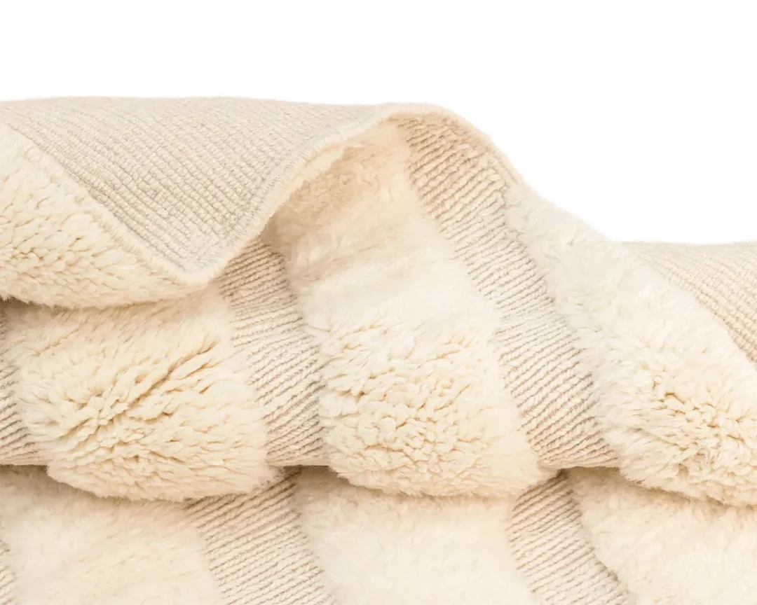 A close-up of a folded cream-colored blanket with alternating textured and fluffy striped patterns.