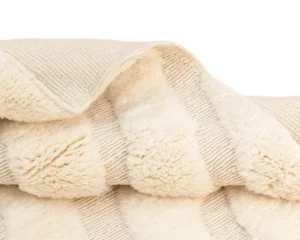 A close-up of a folded cream-colored blanket with alternating textured and fluffy striped patterns.
