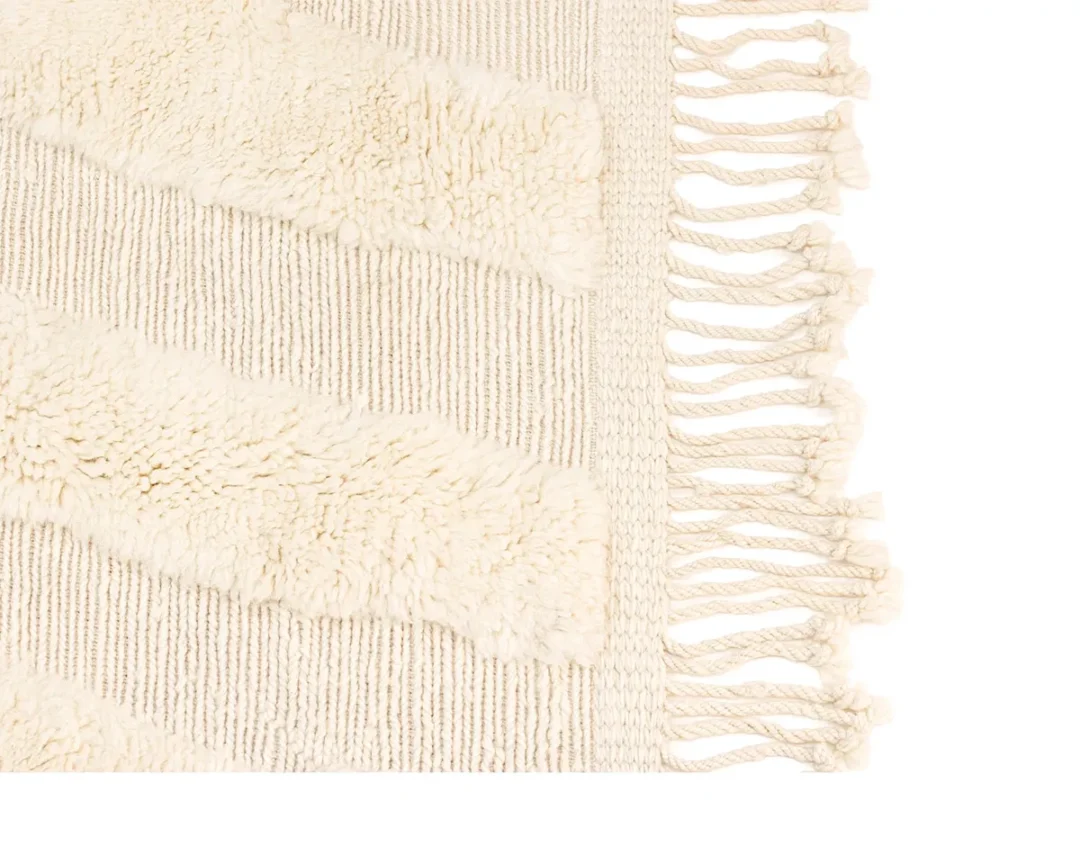 A close-up of a cream-colored woven rug shows textured diagonal stripes and fringed tassels along the edge.