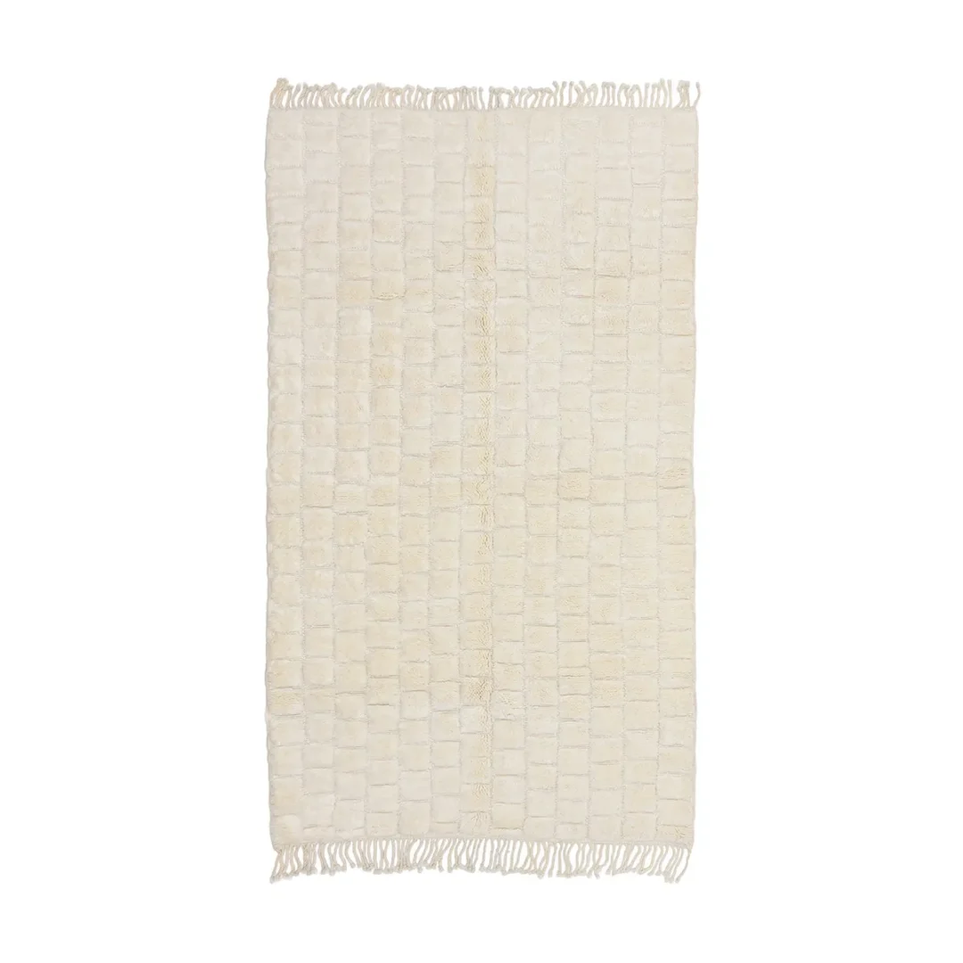 A rectangular, cream-colored rug with a square grid pattern and short fringe on the shorter edges.