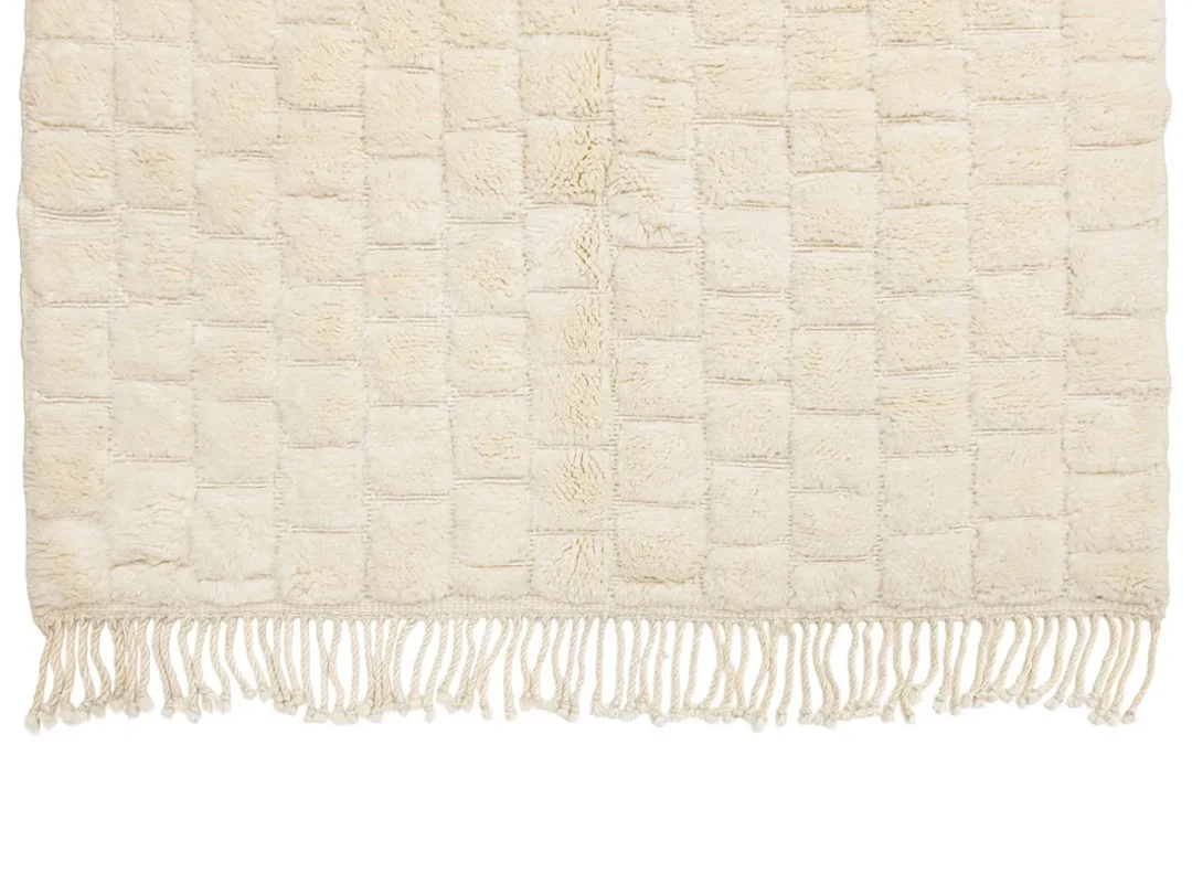 A cream-colored rug with a checkerboard pattern and fringed edges.