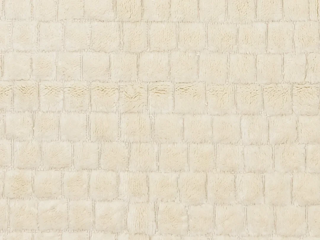 A close-up of a beige, soft-textured fabric with a grid-like, square pattern.