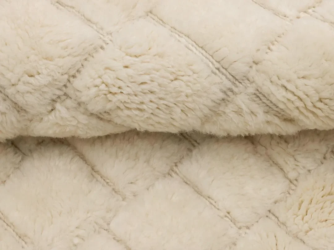 Close-up view of a cream-colored, quilted faux fur fabric with a diamond pattern.