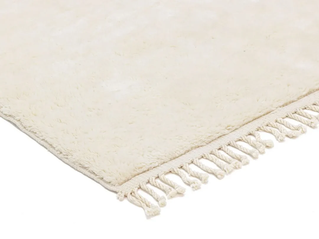 A close-up view of a cream-colored rug with a soft texture and tasseled fringe along the edge.