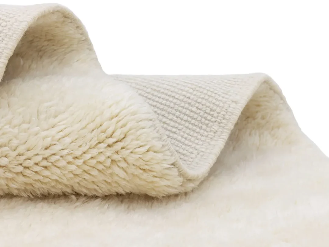 A close-up of a folded beige fabric with a textured woven surface on one side and a soft, fluffy fleece on the other.
