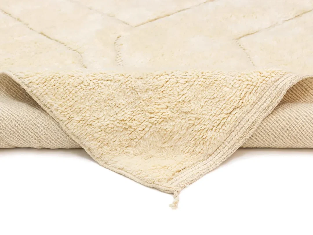 A close-up of a cream-colored textured rug with one corner folded over, showing the underside and edge details.