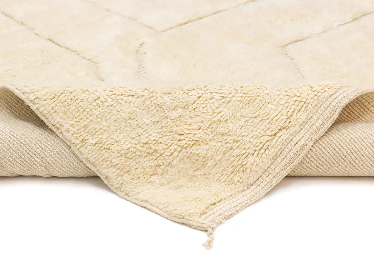 A close-up of a cream-colored textured rug with one corner folded over, showing the underside and edge details.