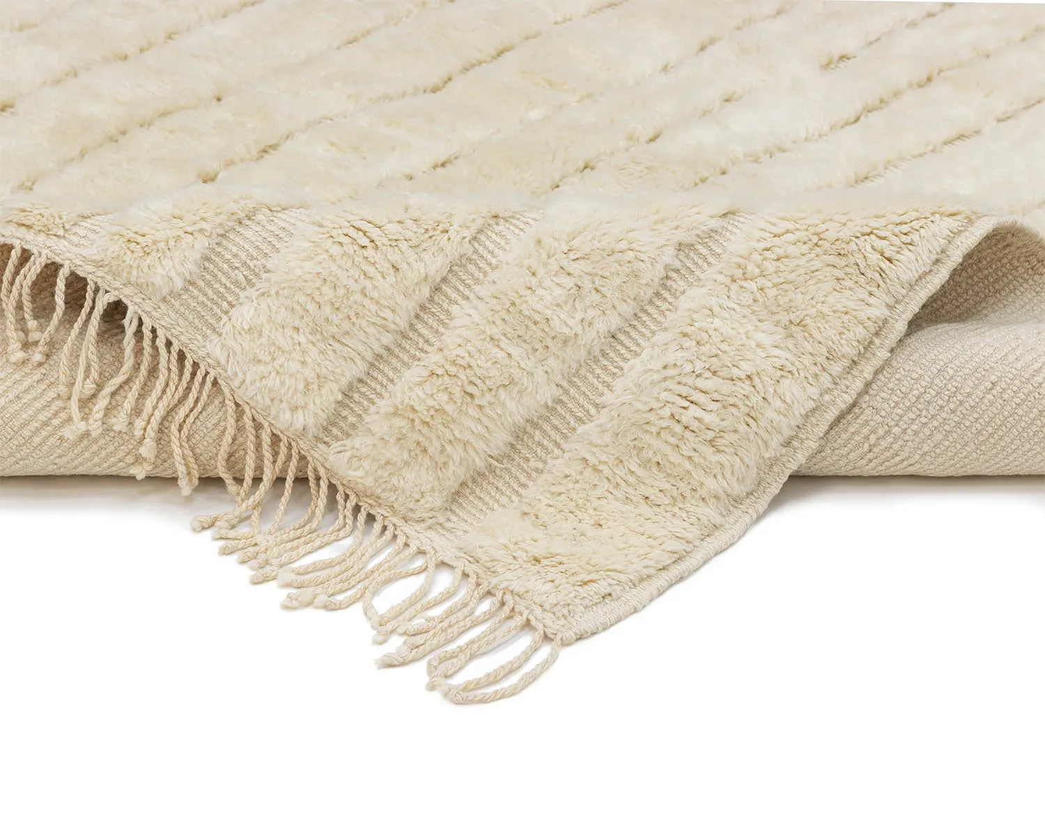 A close-up view of a cream-colored, textured rug with fringe along the edges, partially folded over on a white background.