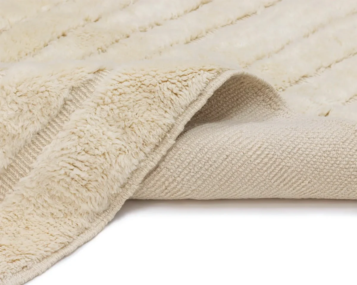 A close-up of a cream-colored, textured blanket or rug with a soft, furry surface and a woven underside partially folded over.