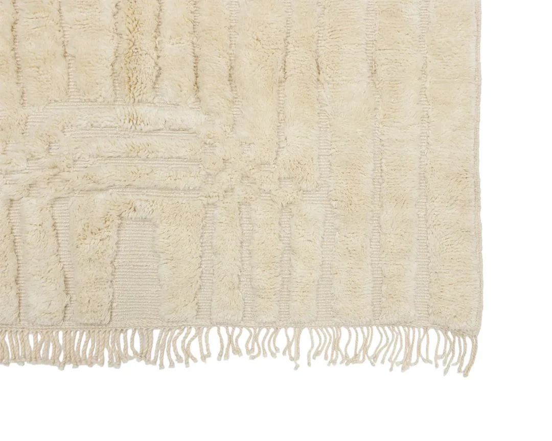 Close-up of a beige textured rug with a subtle pattern and fringe along the bottom edge.