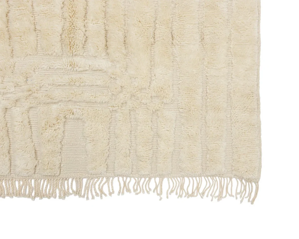 Close-up of a beige textured rug with a subtle pattern and fringe along the bottom edge.