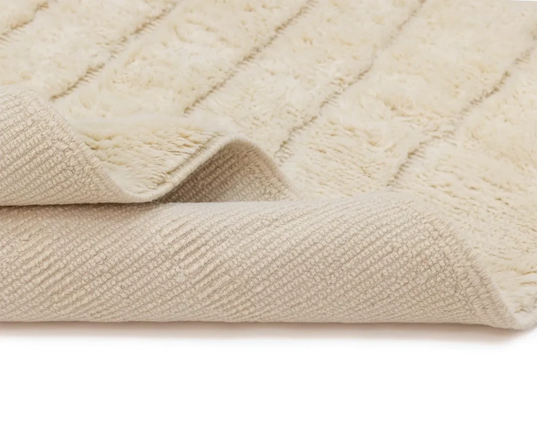 A close-up of a soft, cream-colored textured rug with the corner folded over, showing both the plush surface and the patterned underside.