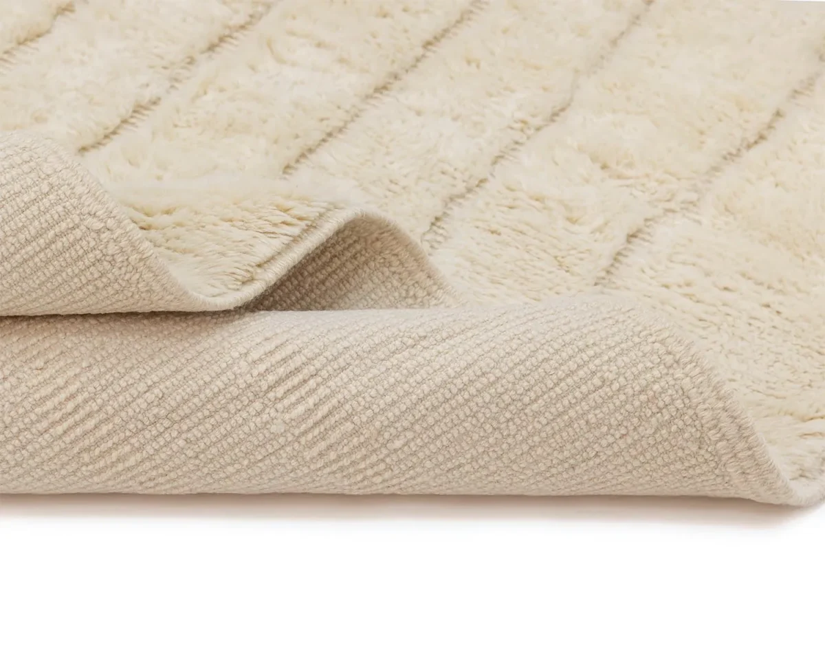 A close-up of a soft, cream-colored textured rug with the corner folded over, showing both the plush surface and the patterned underside.