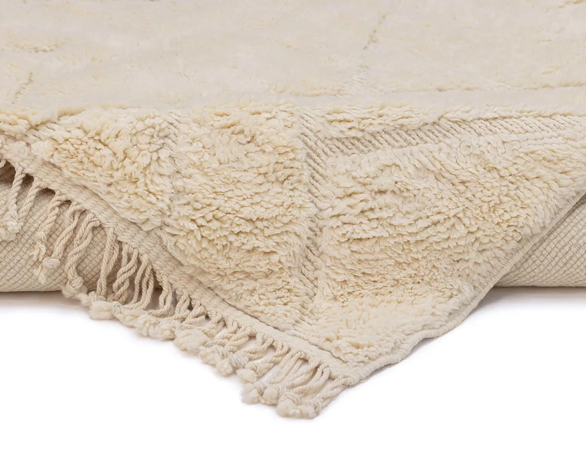 Close-up of a cream-colored textured rug with a fringed edge, showing both the top surface and underside of the material.