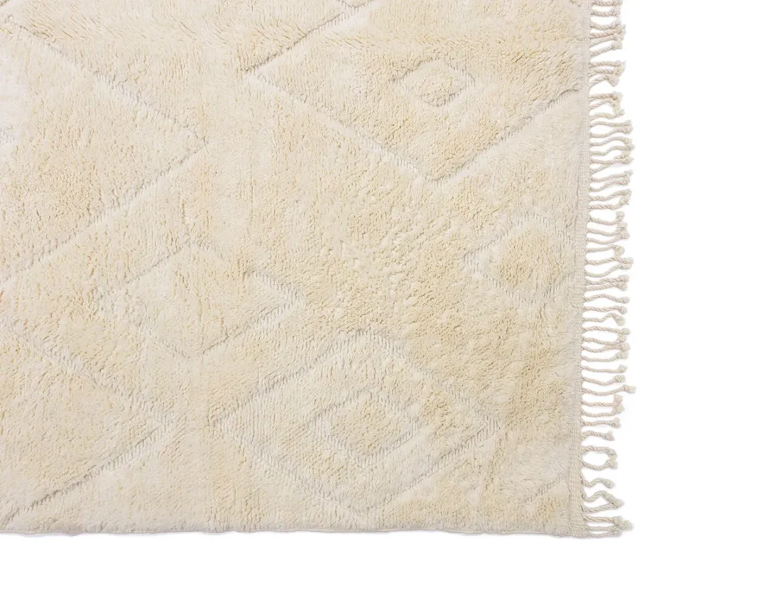 Close-up of a cream-colored textured rug with a geometric pattern and fringed edges on one side.