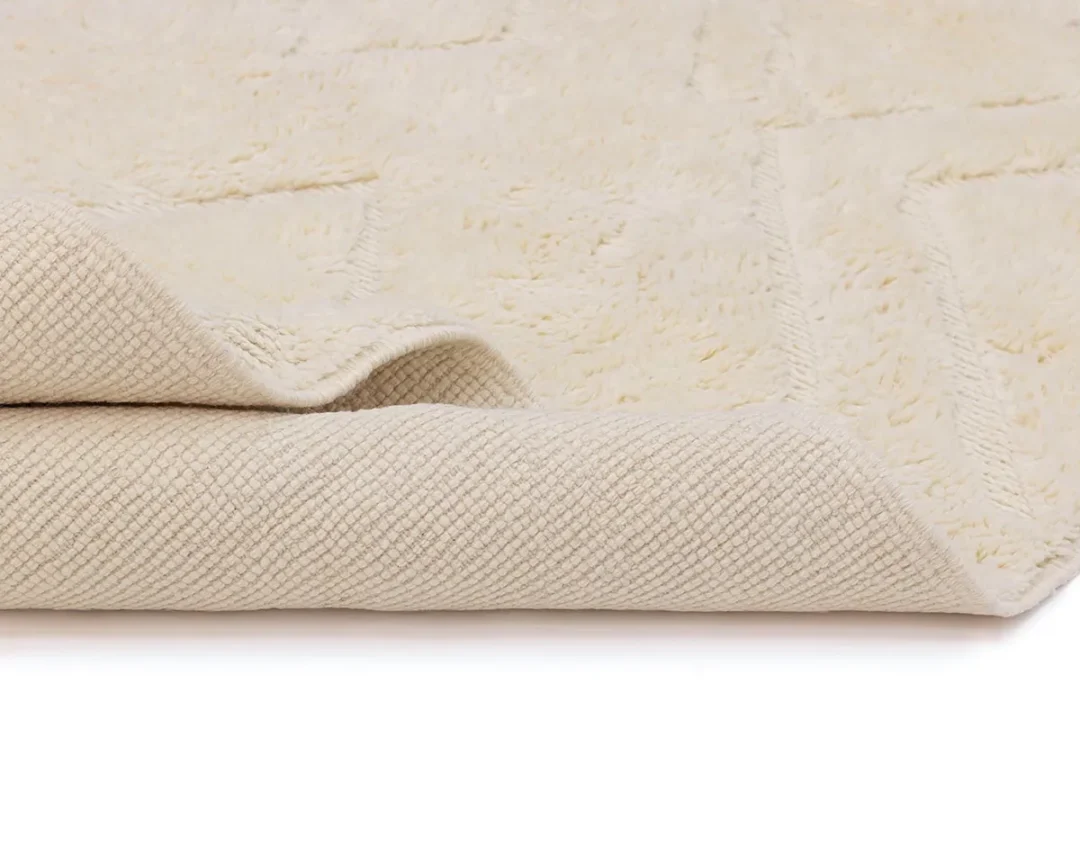 Close-up of a beige textured rug with one corner slightly folded over, showing the underside and surface pattern against a white background.