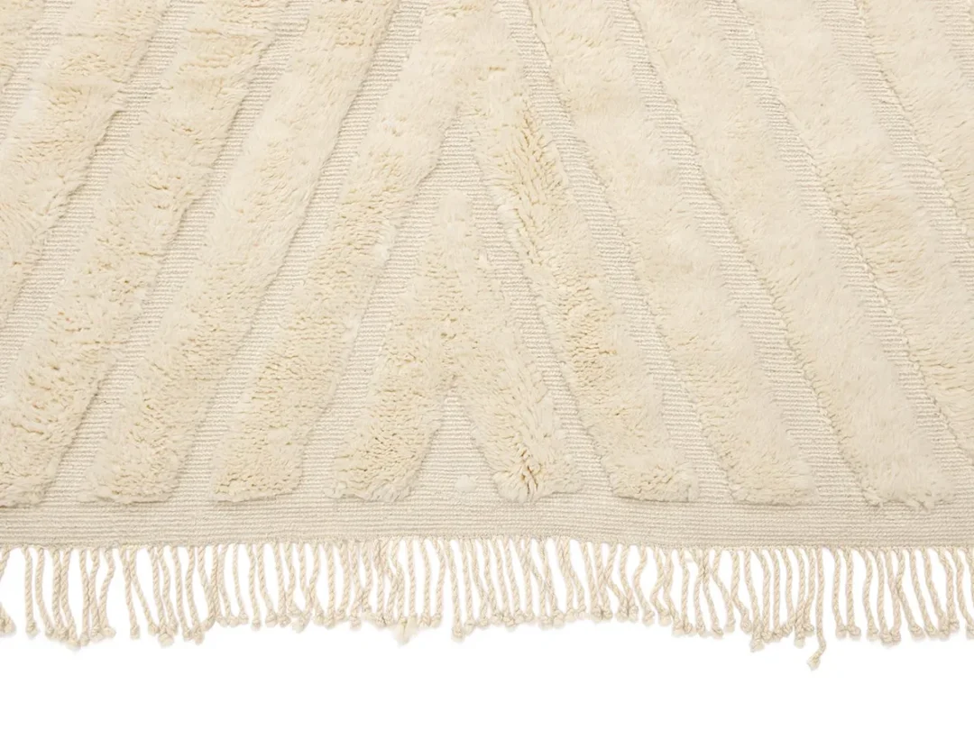 A cream-colored textured rug with raised chevron patterns and fringed tassels along the edge.