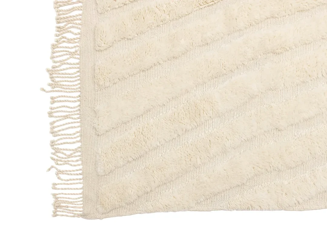 Close-up of a cream-colored textured rug with diagonal patterns and fringe along the edges, shown on a white background.