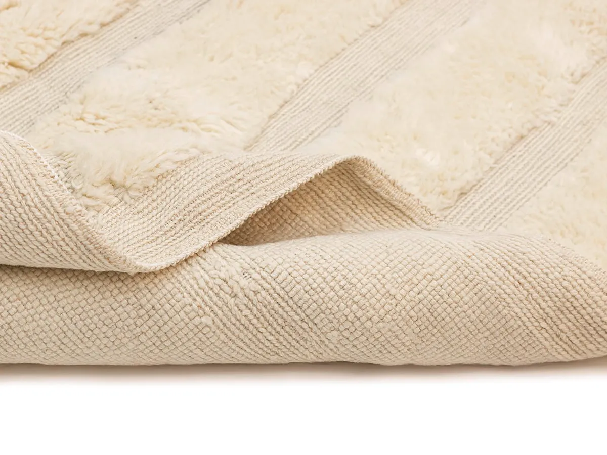 A close-up view of a beige textured rug with raised, soft, fuzzy stripes and a visible woven underside.