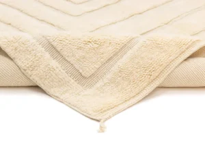 A close-up of a cream-colored textured blanket with a raised chevron pattern and a tassel at the corner.