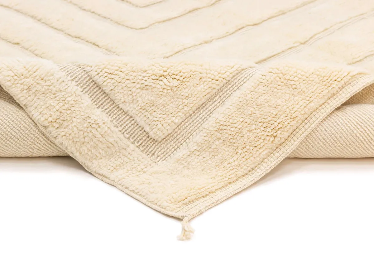A close-up of a cream-colored textured blanket with a raised chevron pattern and a tassel at the corner.