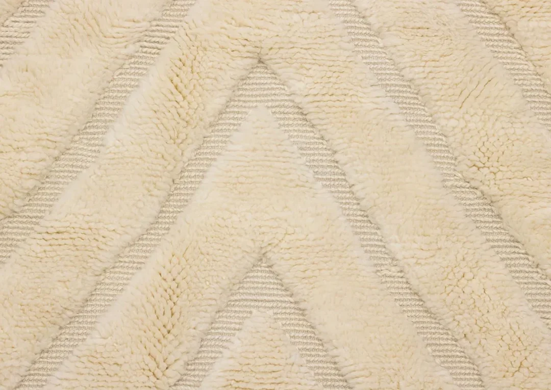 Close-up of a cream-colored textured rug with a chevron pattern formed by alternating raised and flat sections.
