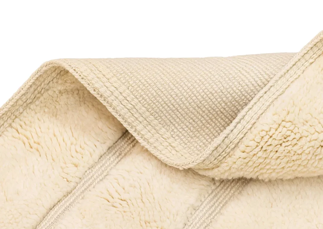 Close-up of a cream-colored fleece blanket partially folded, showing the soft, textured sherpa side and the smooth, woven backside.