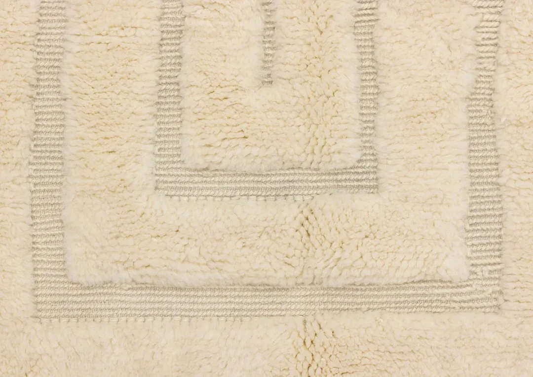 Close-up of a cream-colored textured bath mat with a raised geometric border pattern.