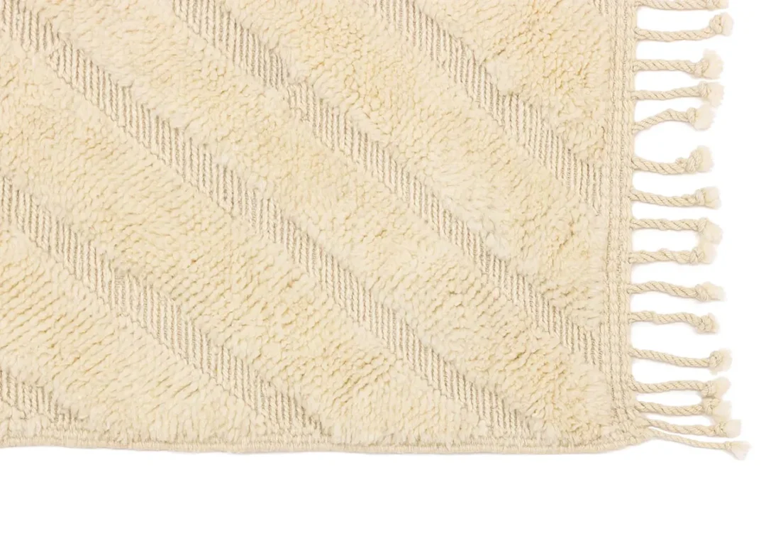 Close-up of a cream-colored textured rug with diagonal stripe pattern and fringed tassels on the edge.