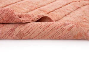 A close-up of an orange textured rug with one corner folded over, showing the underside and surface details, set against a white background.