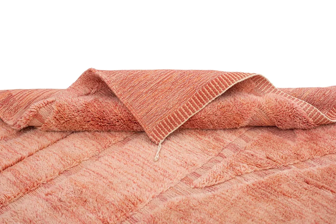 A folded, textured coral-colored blanket with a visible edge and fringe, displayed on a white background.