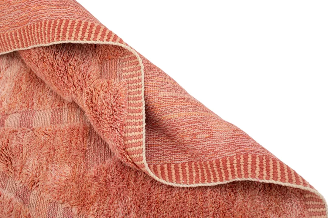 A close-up of a folded terracotta-colored towel with a striped border and textured surface.