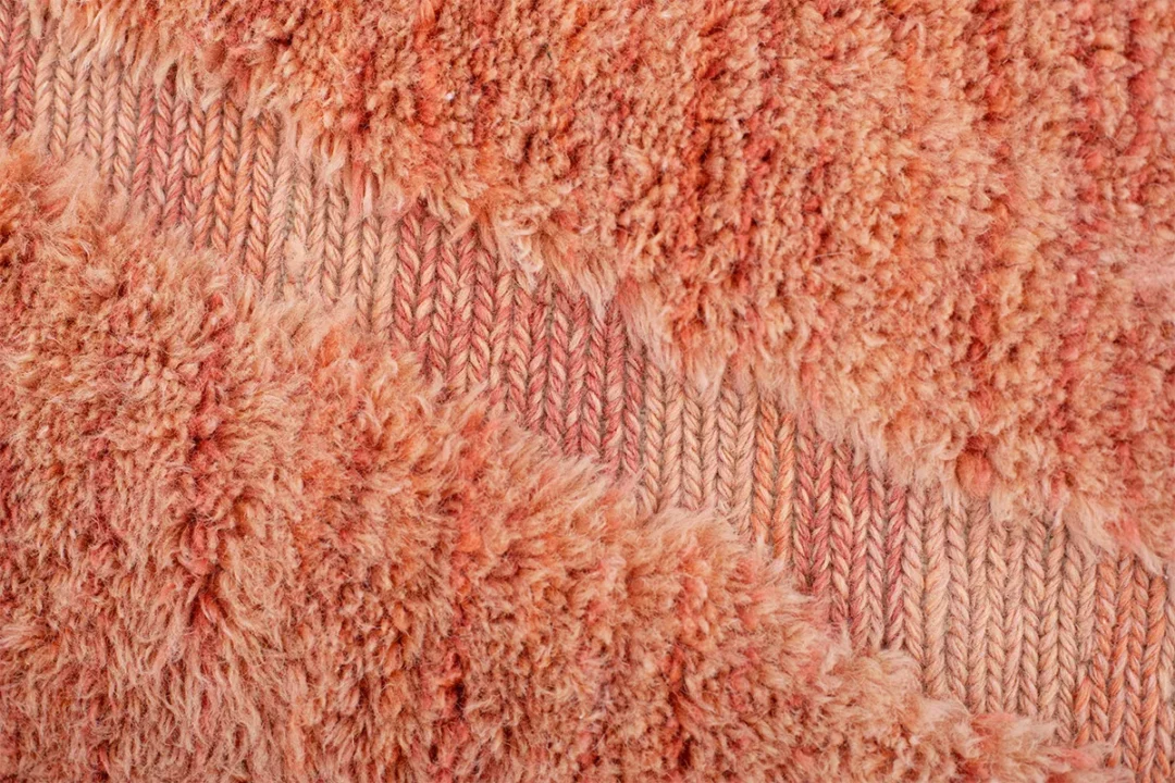 Close-up of a textured fabric with alternating sections of fluffy and tightly knitted coral-colored yarn.