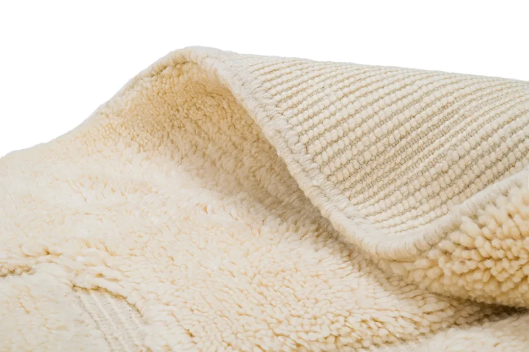 A close-up view of a cream-colored textured rug, showing both the soft, fluffy side and the ribbed underside.