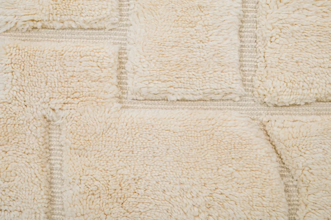 Close-up of a cream-colored, textured rug with rectangular sections separated by visible seams.