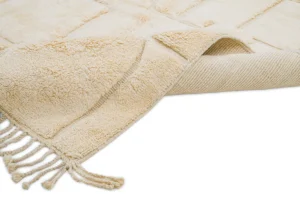 A beige textured rug with fringe on one end is partially folded over, showing its underside and woven backing.