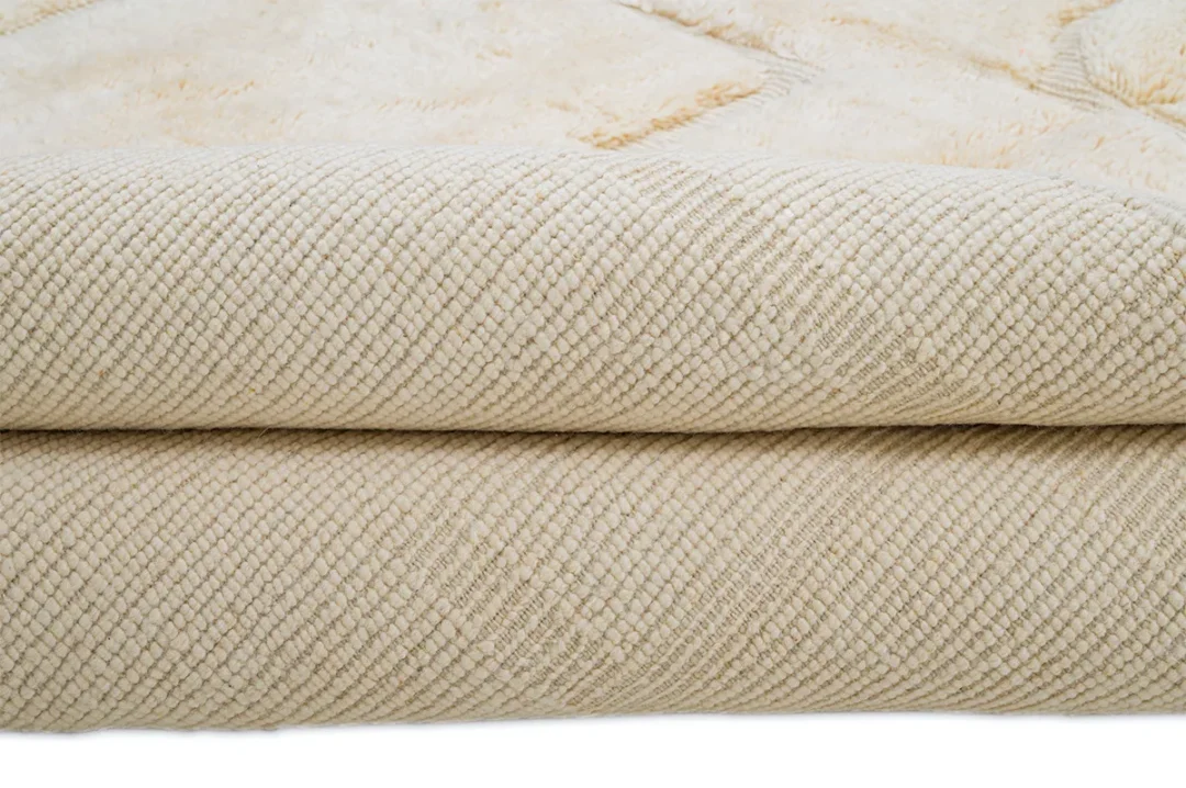 Close-up of a folded beige textured rug, showing a subtle diamond pattern on the surface.