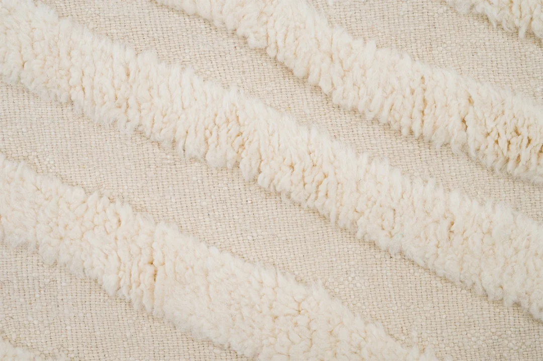 Close-up of a textured rug with diagonal rows of thick, soft, cream-colored tufts on a woven background.